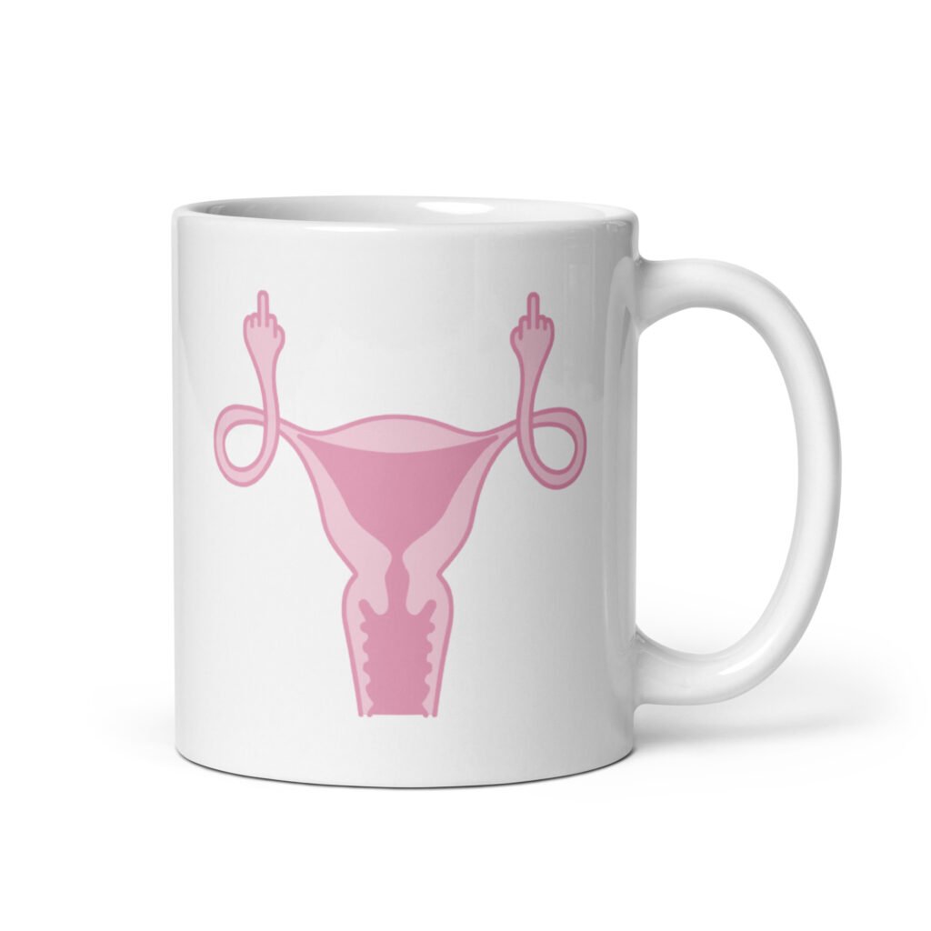 White ceramic coffee mug with with image of a pink uterus flipping middle finger graphic printed on both sides.