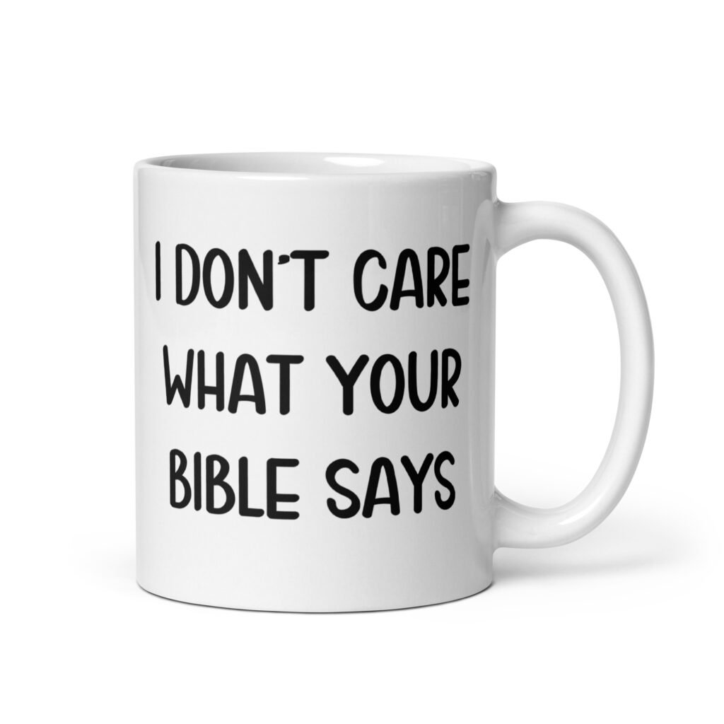 White ceramic coffee mug with the text 'I don't care what your bible says' printed on both sides.
