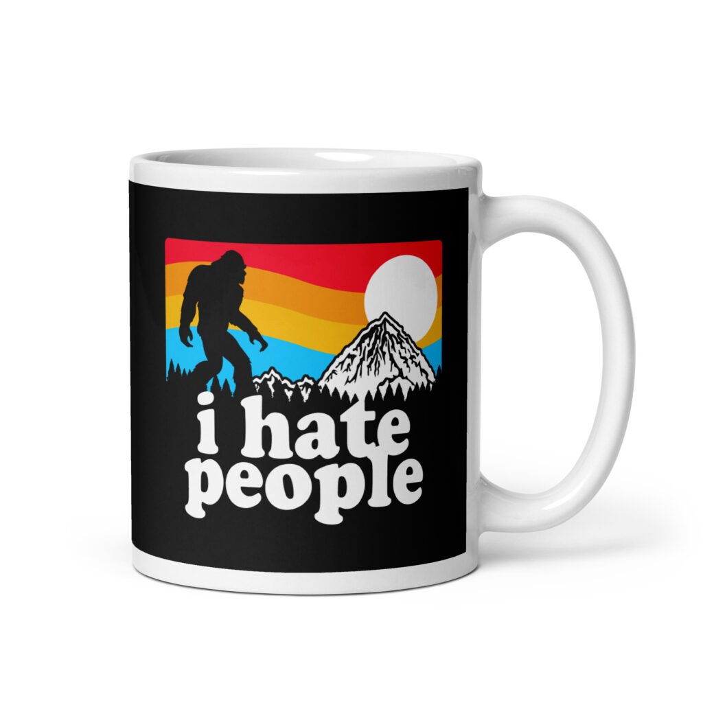 White coffee mug with graphic of Bigfoot walking into the sunset with the text 'I hate people' printed on both sides.