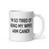 White ceramic coffee mug with the funny phrase 'I'm so tired of being my wife's arm candy' printed on both sides.