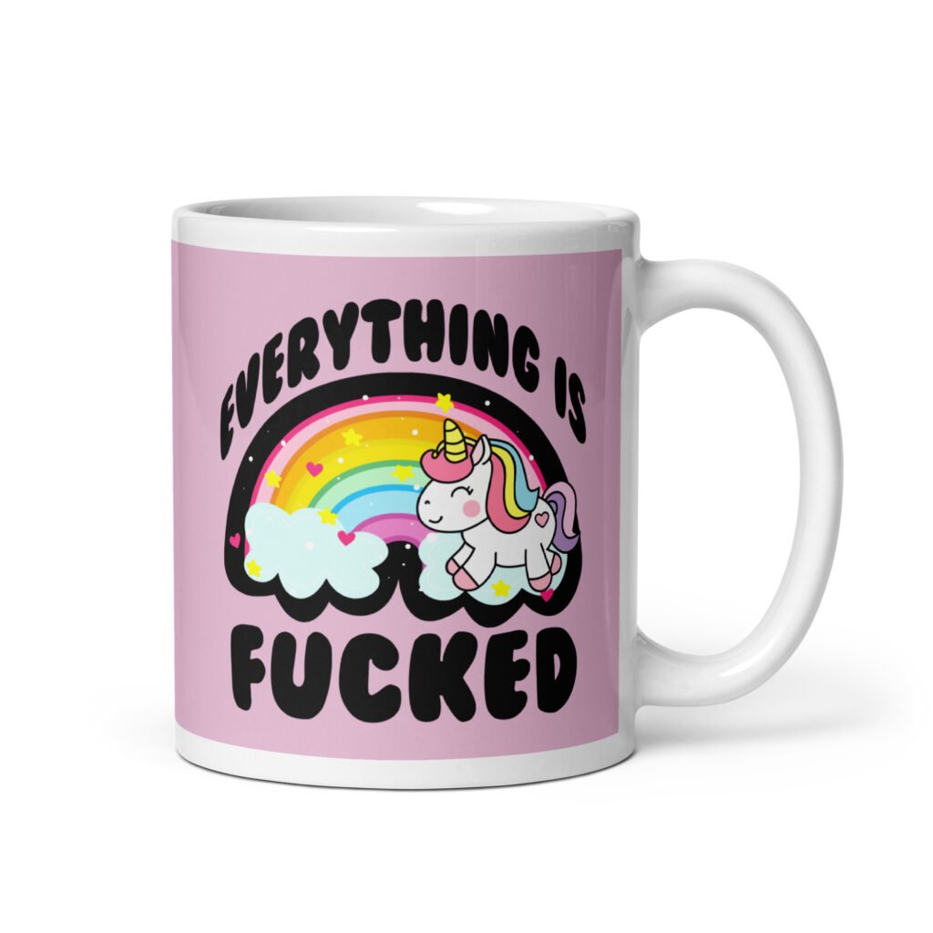 Pink and white ceramic coffee mug with a graphic of a kawaii style unicorn and a pastel rainbow with the text 'Everything is fucked' printed on both sides. The background is pink.