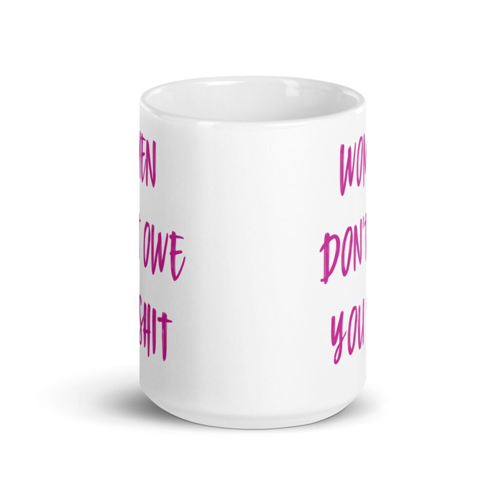 White ceramic coffee mug with the words 'Women don't owe you shit' printed on both sides in pink.
