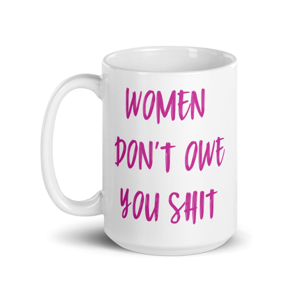 White ceramic coffee mug with the words 'Women don't owe you shit' printed on both sides in pink.