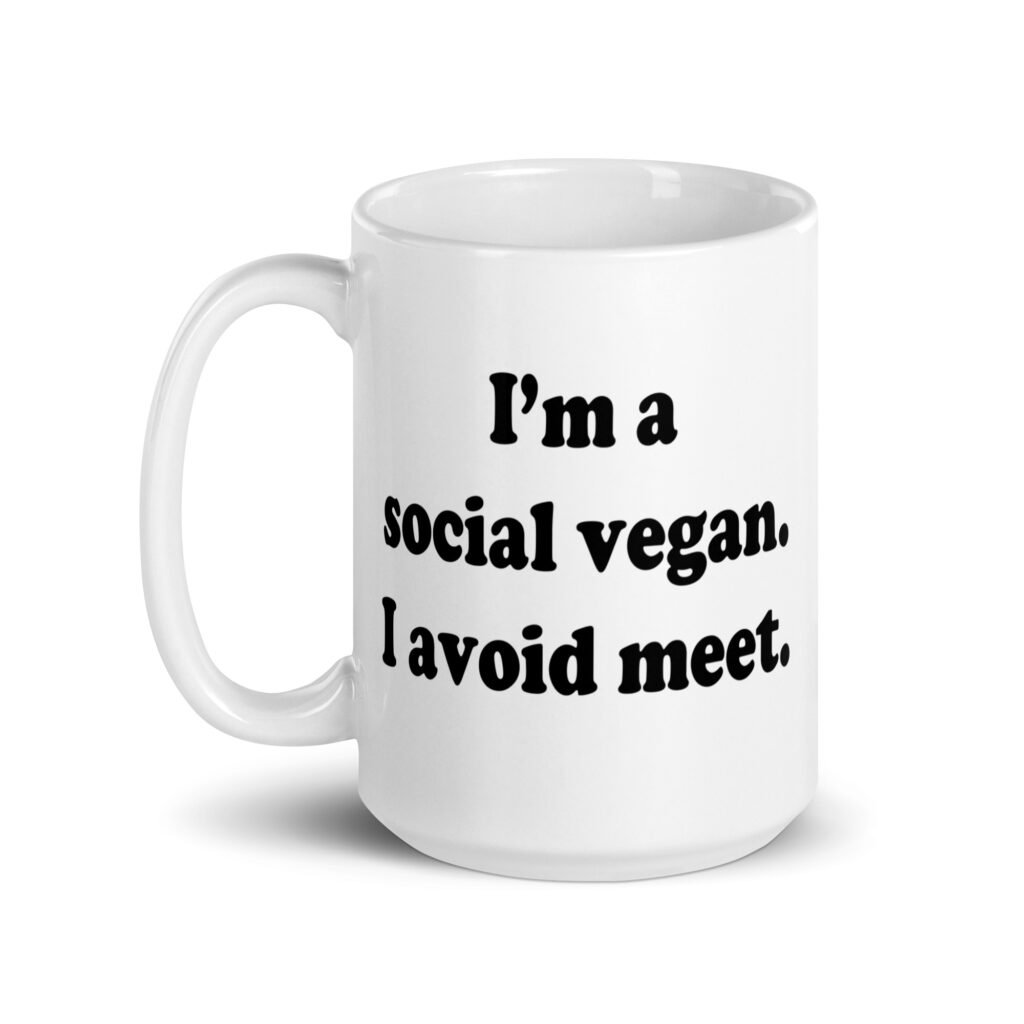 White ceramic mug with the pun phrase 'I'm a social vegan. I avoid meet.' printed on both sides.