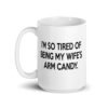 White ceramic coffee mug with the funny phrase 'I'm so tired of being my wife's arm candy' printed on both sides.