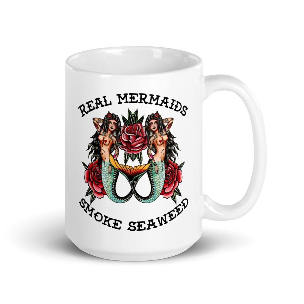 White ceramic mug with image of 2 mermaids and the text 'Real mermaids smoke seaweed' printed on both sides.