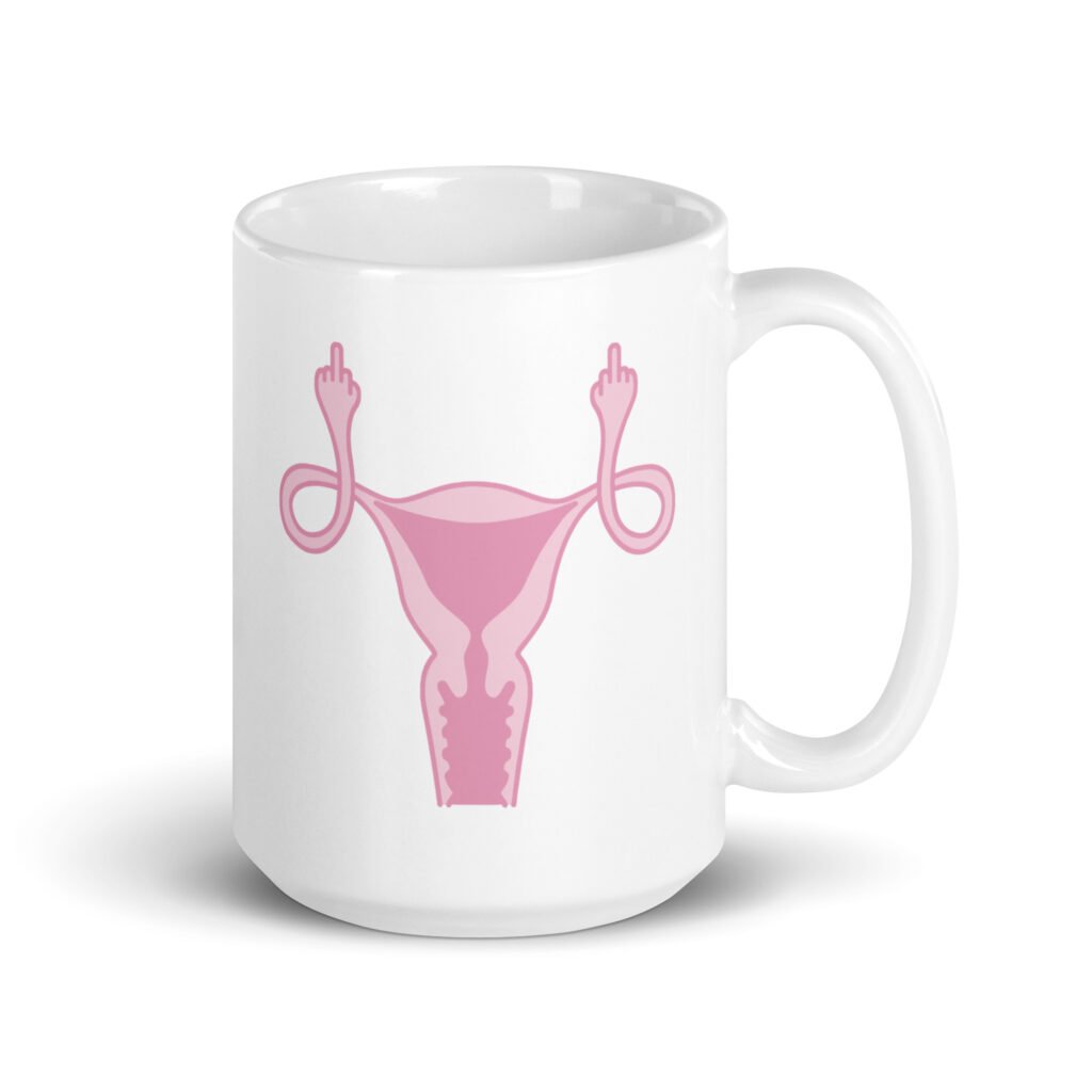 White ceramic coffee mug with with image of a pink uterus flipping middle finger graphic printed on both sides.