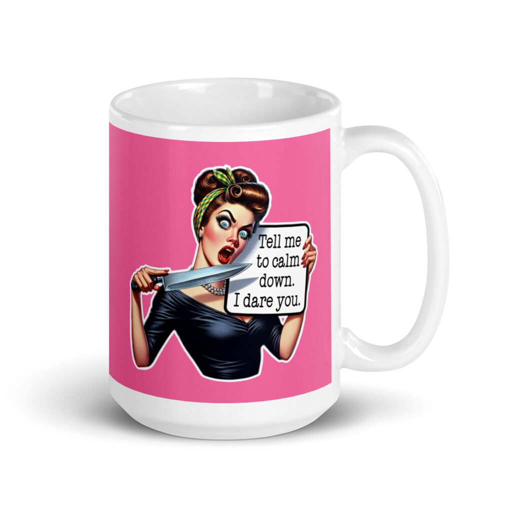 White ceramic coffee mug with pink color wrapped around. The mug has a graphic of an angry looking retro woman holding a knife and a sign. The sign says 'Tell me to calm down. I dare you.' The graphic is printed on both sides of the mug.