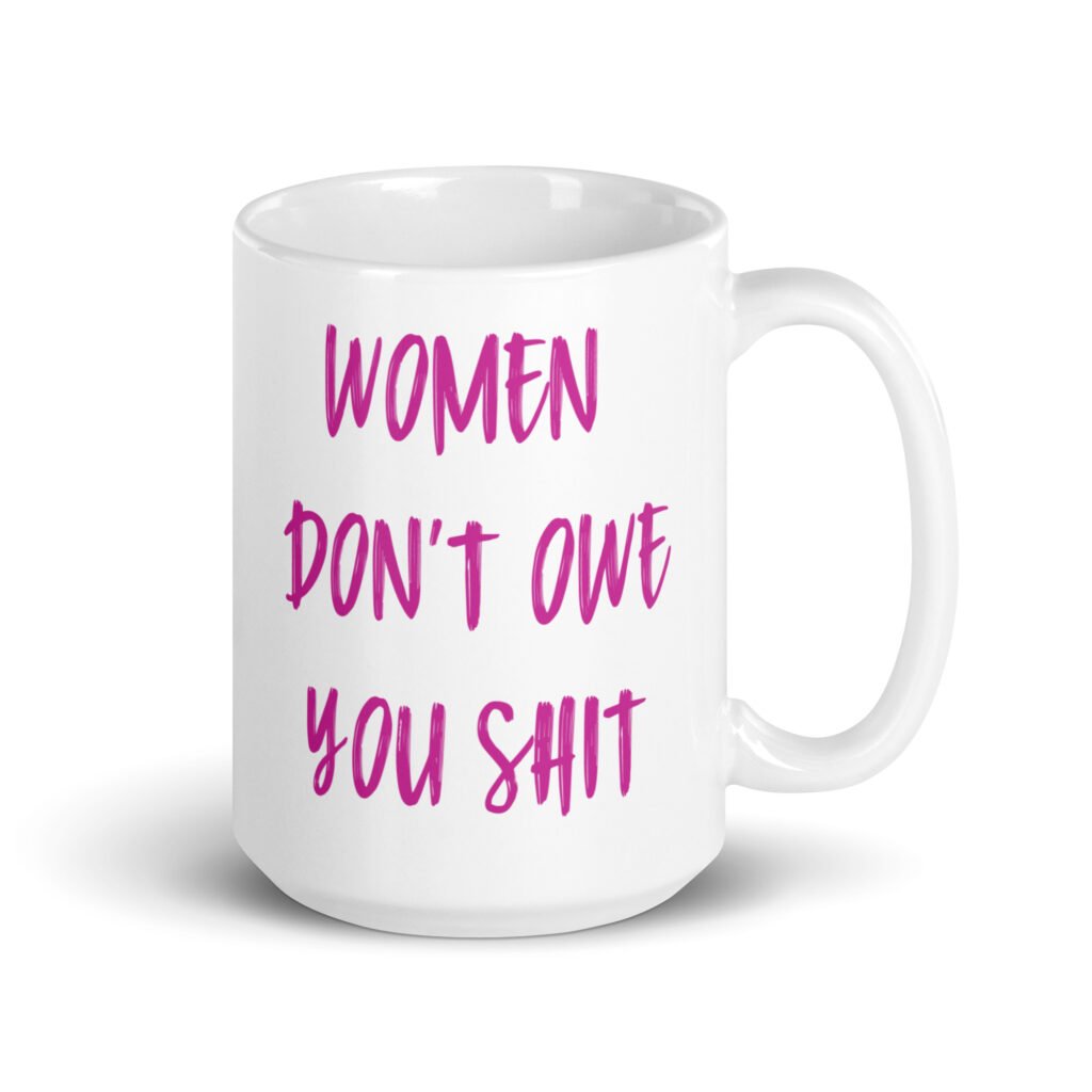 White ceramic coffee mug with the words 'Women don't owe you shit' printed on both sides in pink.