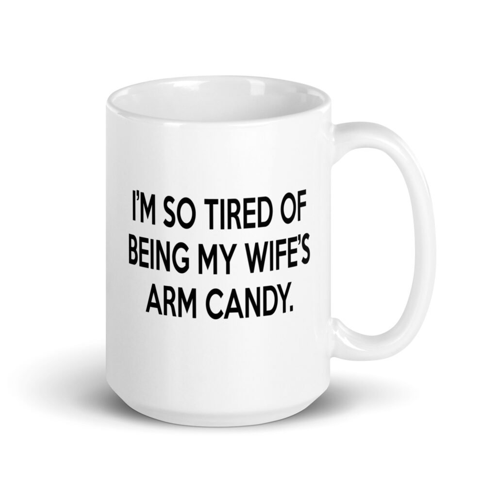 White ceramic coffee mug with the funny phrase 'I'm so tired of being my wife's arm candy' printed on both sides.