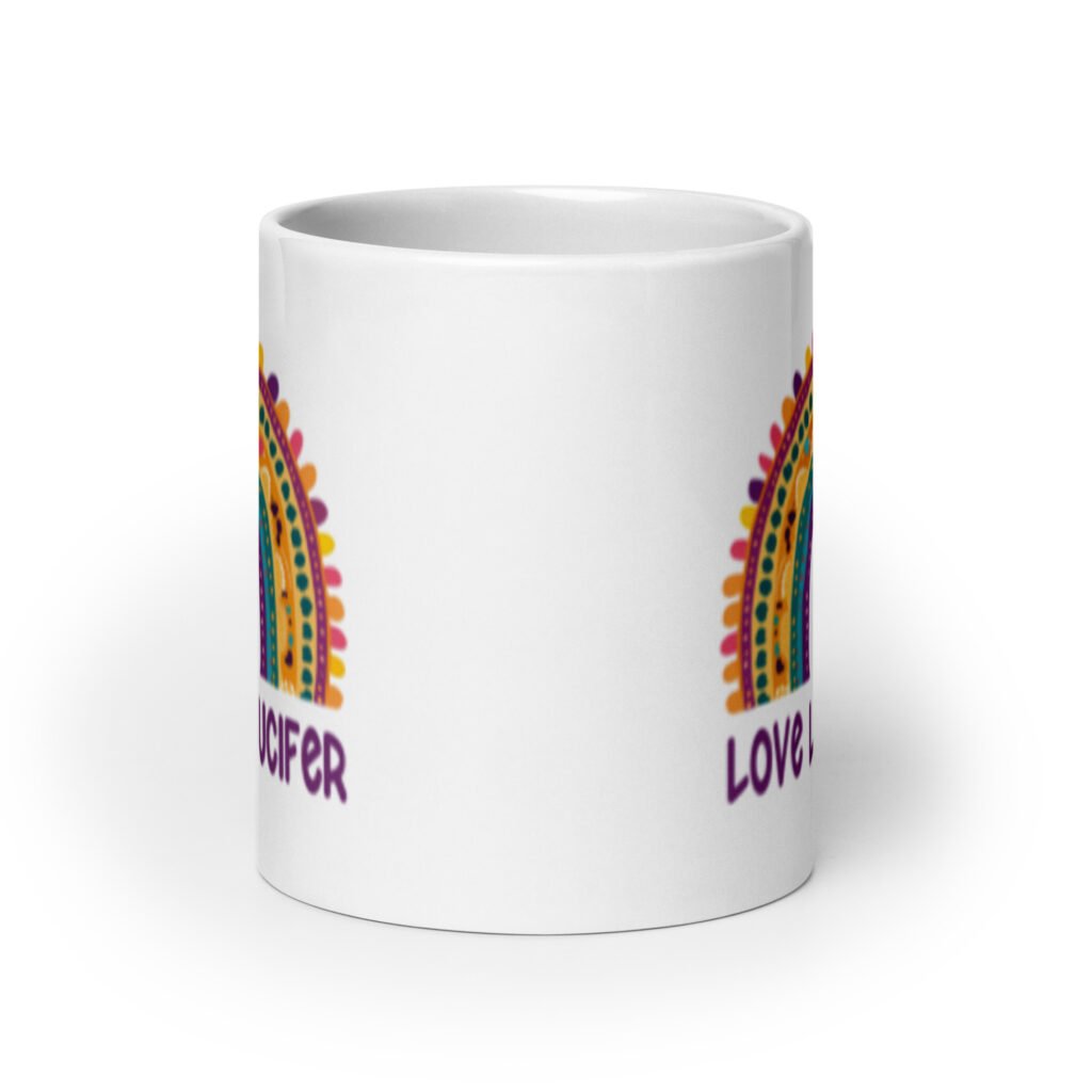 White ceramic mug with an image of a boho style rainbow. There is an upside down cross in the center arch of the rainbow and the text 'Love like Lucifer' printed under. The graphics are printed on both sides of the mug.