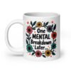 White ceramic mug with a multi color floral wreath design printed on both sides. The words 'One mental breakdown later...' are printed in the center of the wreath.