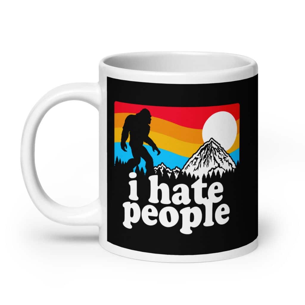 White coffee mug with graphic of Bigfoot walking into the sunset with the text 'I hate people' printed on both sides.