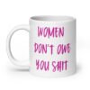 White ceramic coffee mug with the words 'Women don't owe you shit' printed on both sides in pink.