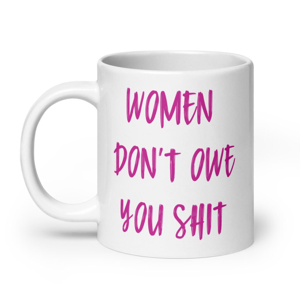 White ceramic coffee mug with the words 'Women don't owe you shit' printed on both sides in pink.