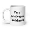 White ceramic mug with the pun phrase 'I'm a social vegan. I avoid meet.' printed on both sides.
