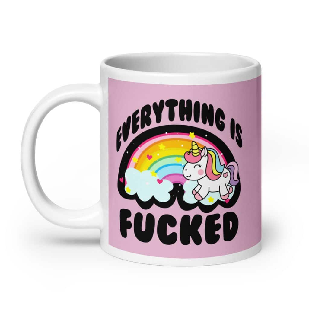 Pink and white ceramic coffee mug with a graphic of a kawaii style unicorn and a pastel rainbow with the text 'Everything is fucked' printed on both sides. The background is pink.