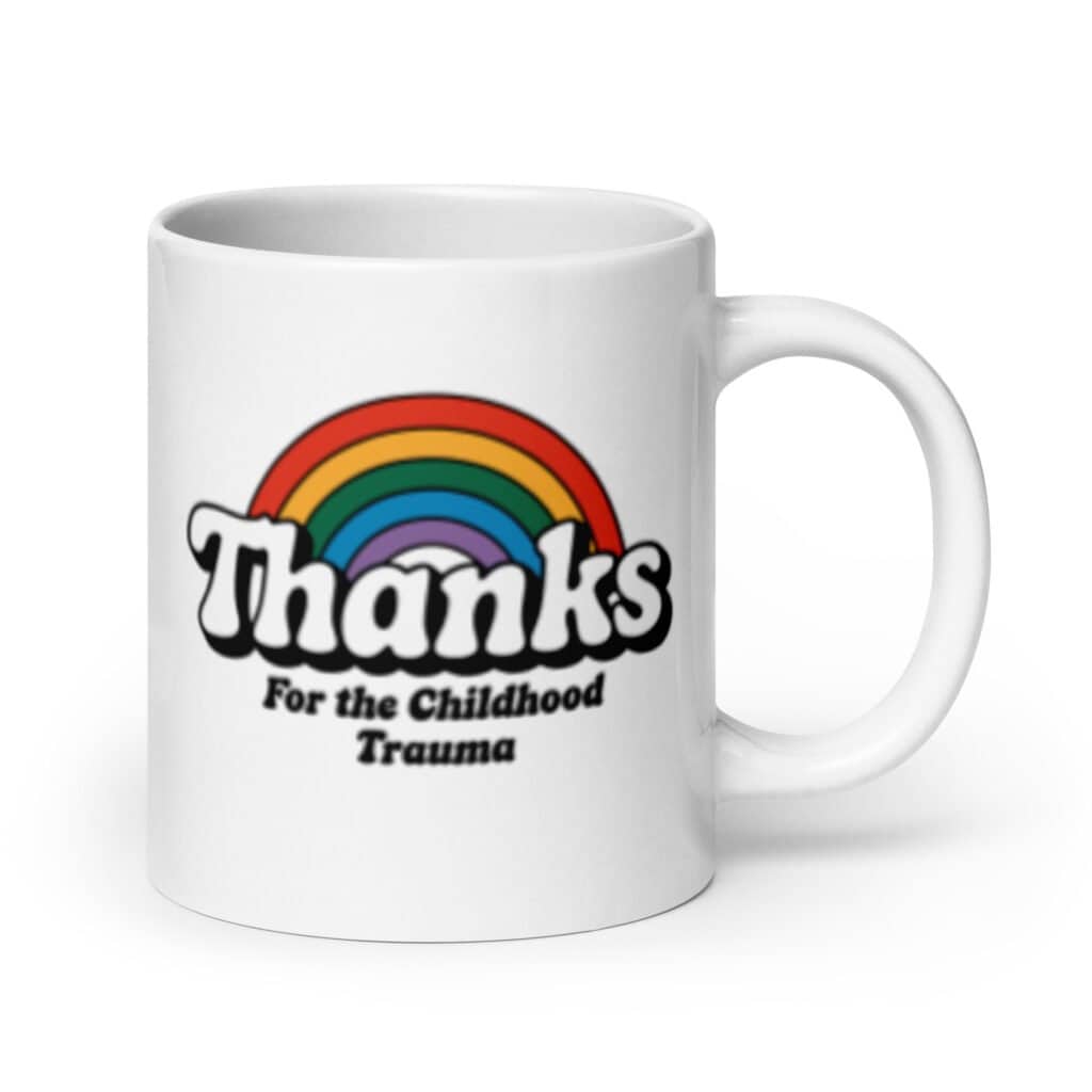 White ceramic mug with an image of a rainbow and the words 'Thanks for the childhood trauma' printed on both sides. The word Thanks is large and the rest of the words are smaller under.