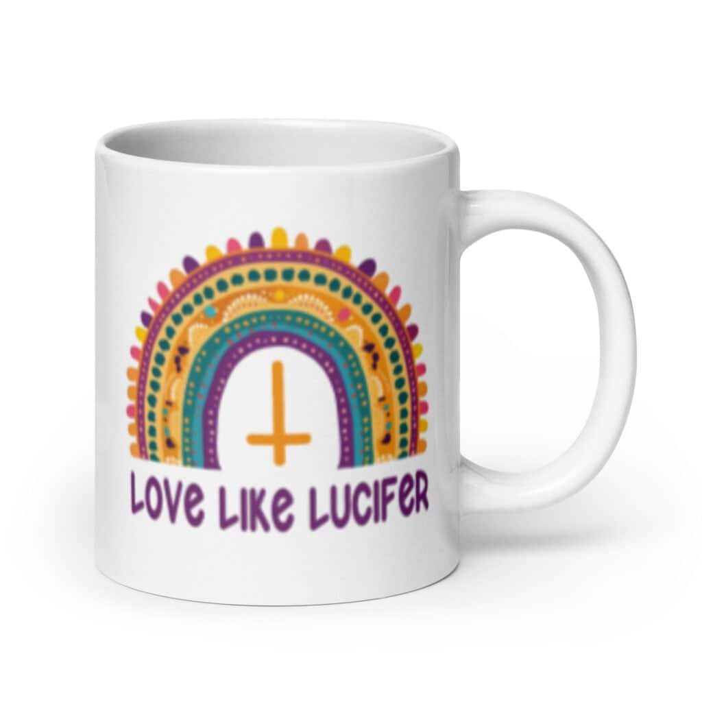 White ceramic mug with an image of a boho style rainbow. There is an upside down cross in the center arch of the rainbow and the text 'Love like Lucifer' printed under. The graphics are printed on both sides of the mug.