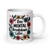 White ceramic mug with a multi color floral wreath design printed on both sides. The words 'One mental breakdown later...' are printed in the center of the wreath.