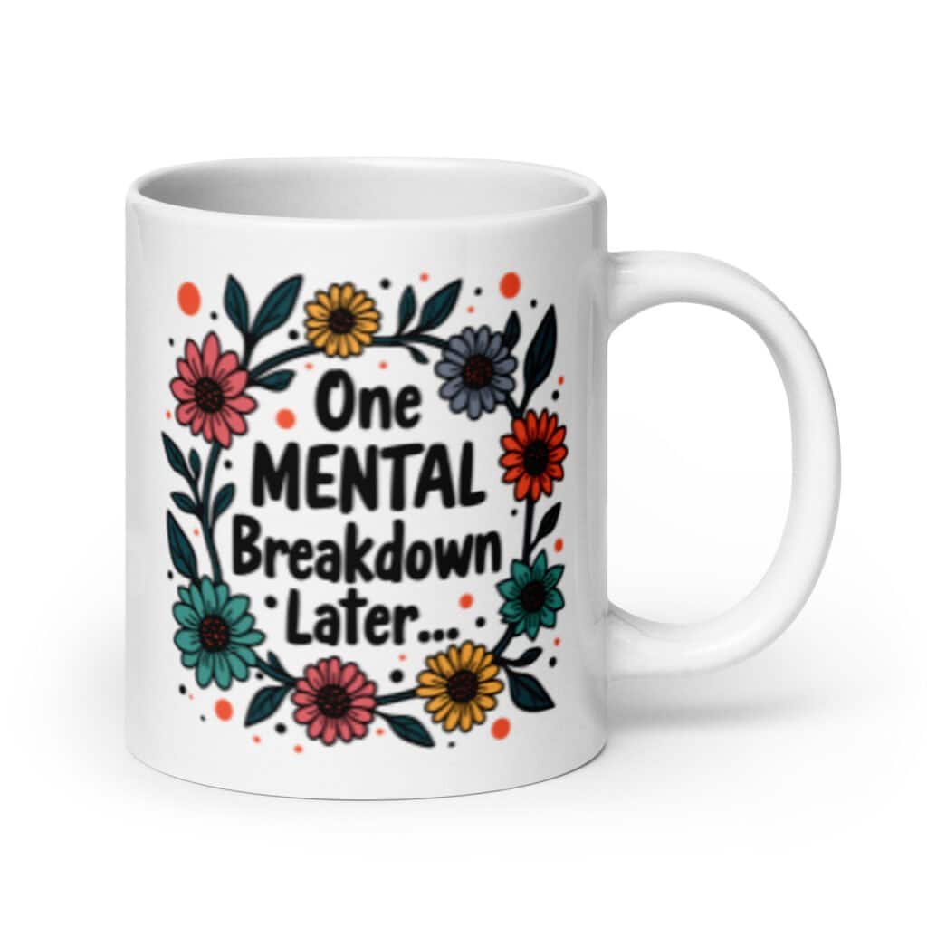 White ceramic mug with a multi color floral wreath design printed on both sides. The words 'One mental breakdown later...' are printed in the center of the wreath.