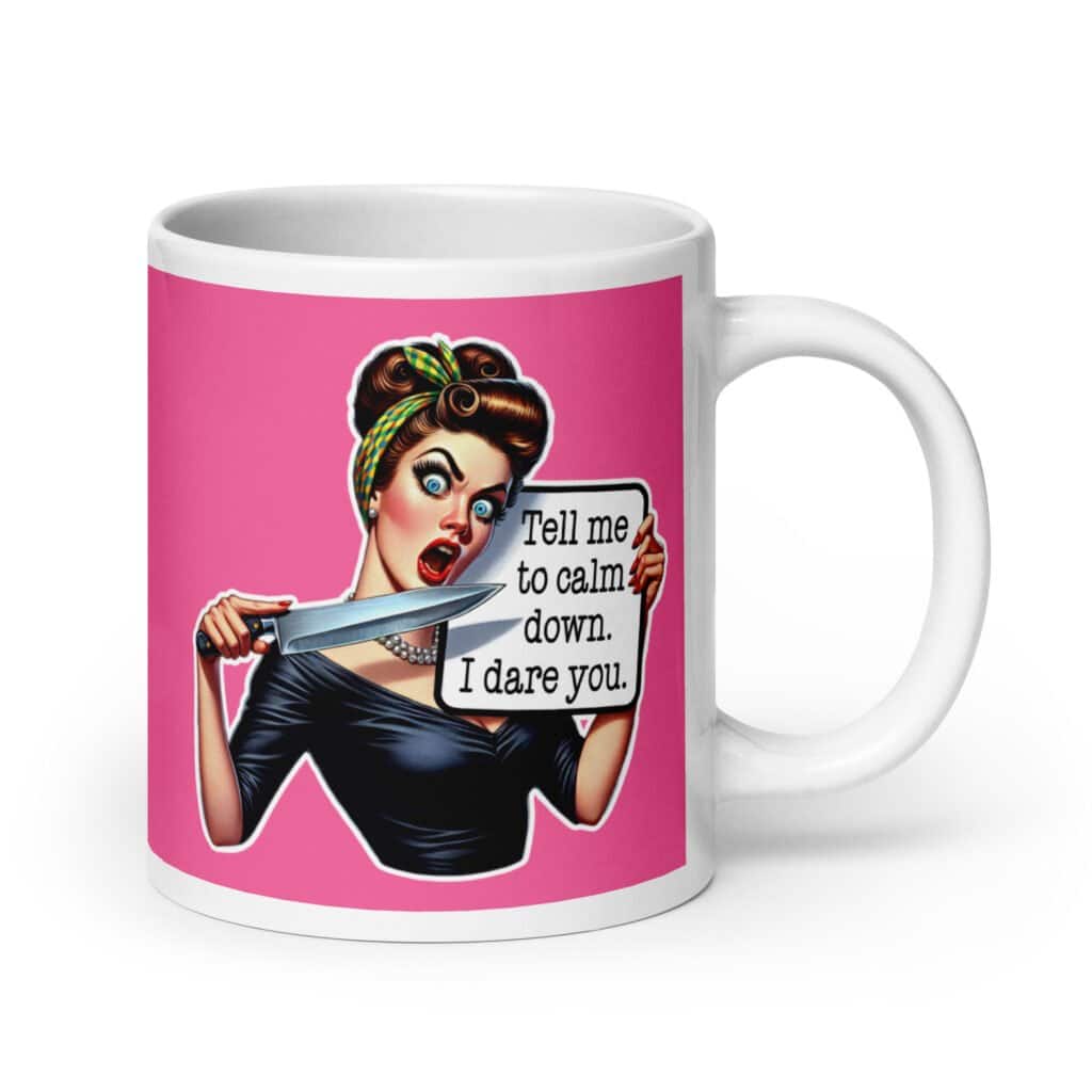 White ceramic coffee mug with pink color wrapped around. The mug has a graphic of an angry looking retro woman holding a knife and a sign. The sign says 'Tell me to calm down. I dare you.' The graphic is printed on both sides of the mug.