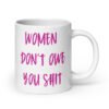 White ceramic coffee mug with the words 'Women don't owe you shit' printed on both sides in pink.
