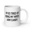 White ceramic coffee mug with the funny phrase 'I'm so tired of being my wife's arm candy' printed on both sides.
