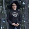 Woman dressed as a witch wearing a black hoodie sweatshirt with image of a pentagram and the text 'I'll pray for you' printed on the front.
