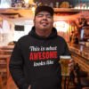 Man holding a beer wearing a black hoodie sweatshirt with the text 'This is what awesome looks like' printed on the front.
