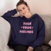 Woman wearing a navy blue hoodie sweatshirt with the text 'Fuck your feelings' printed on the front in pink. There are cute pink hearts next to the words.