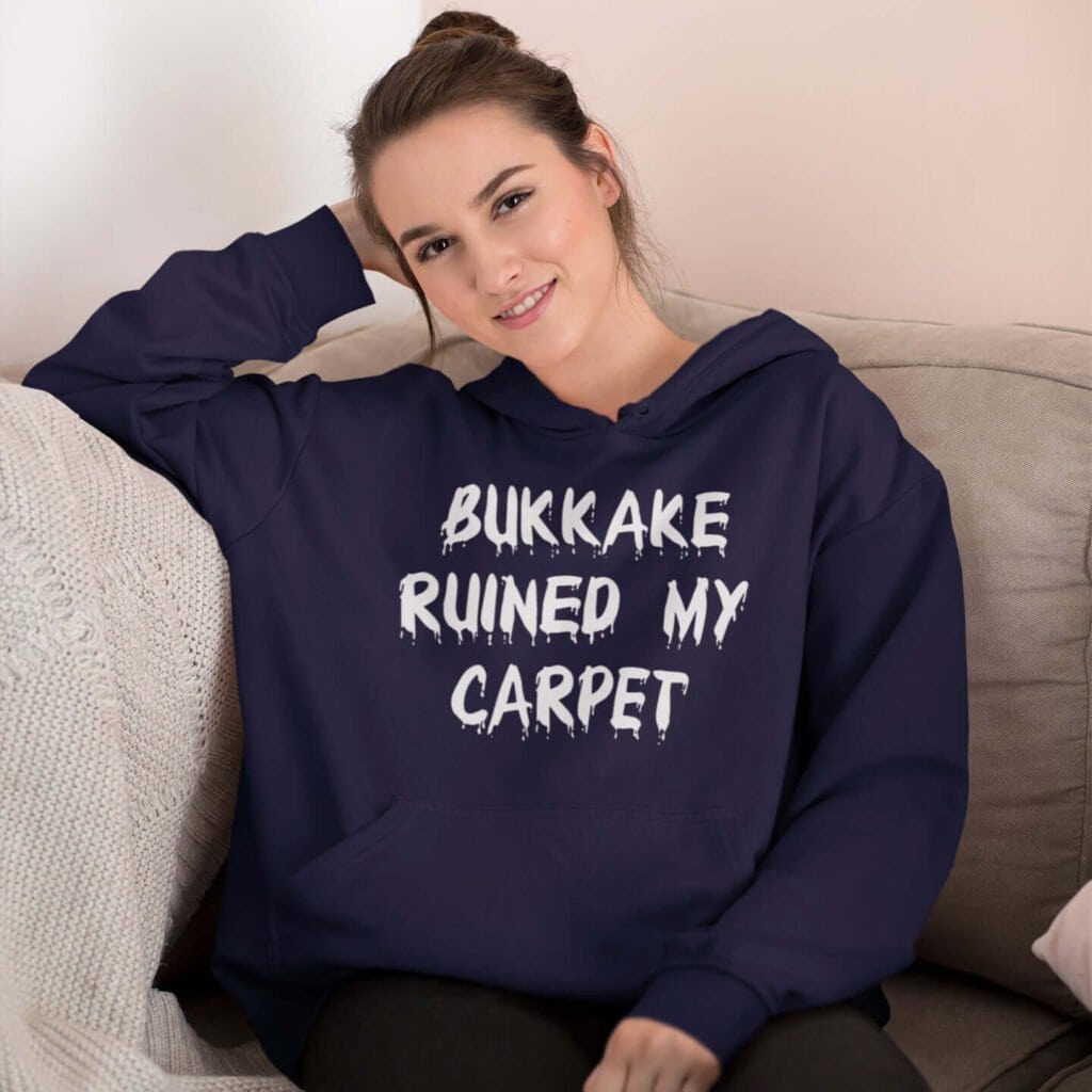 Woman wearing a navy blue hoodie sweatshirt with the text 'Bukkake ruined my carpet' in drippy font printed on the front.