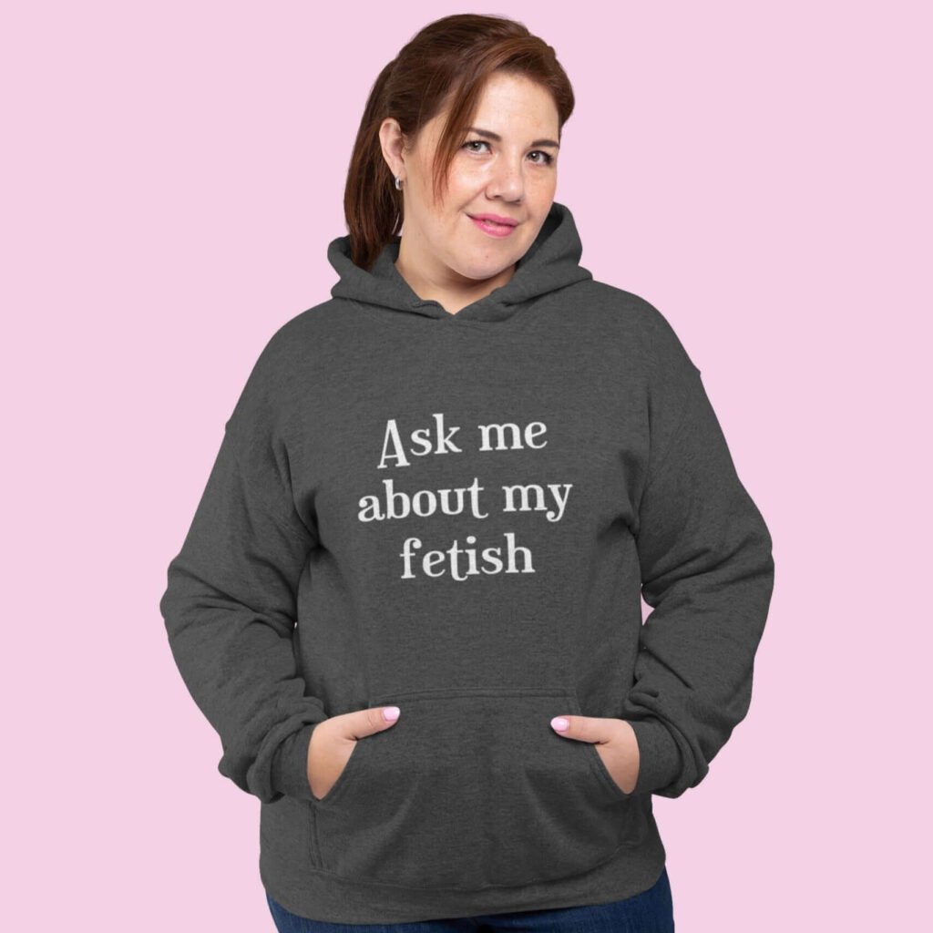 Woman wearing dark grey hoodie sweatshirt with the text 'Ask me about my fetish' printed on the front.