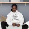 Man sitting on a bed wearing a white hoodie sweatshirt with the phrase It only seems kinky the first time printed on the front. There is an image of handcuffs with the text.