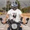 Man riding a motorcycle wearing a white average cock t-shirt with image of a rooster with the word 'Average' printed above.