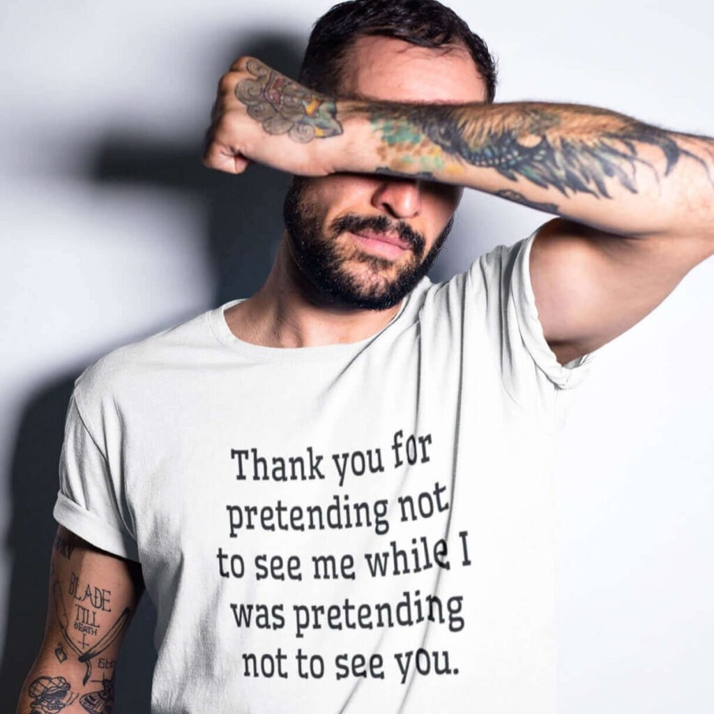 Man covering his eyes while wearing a white t-shirt with the text 'Thank you for pretending not to see me while I was pretending not to see you.' printed on the front.