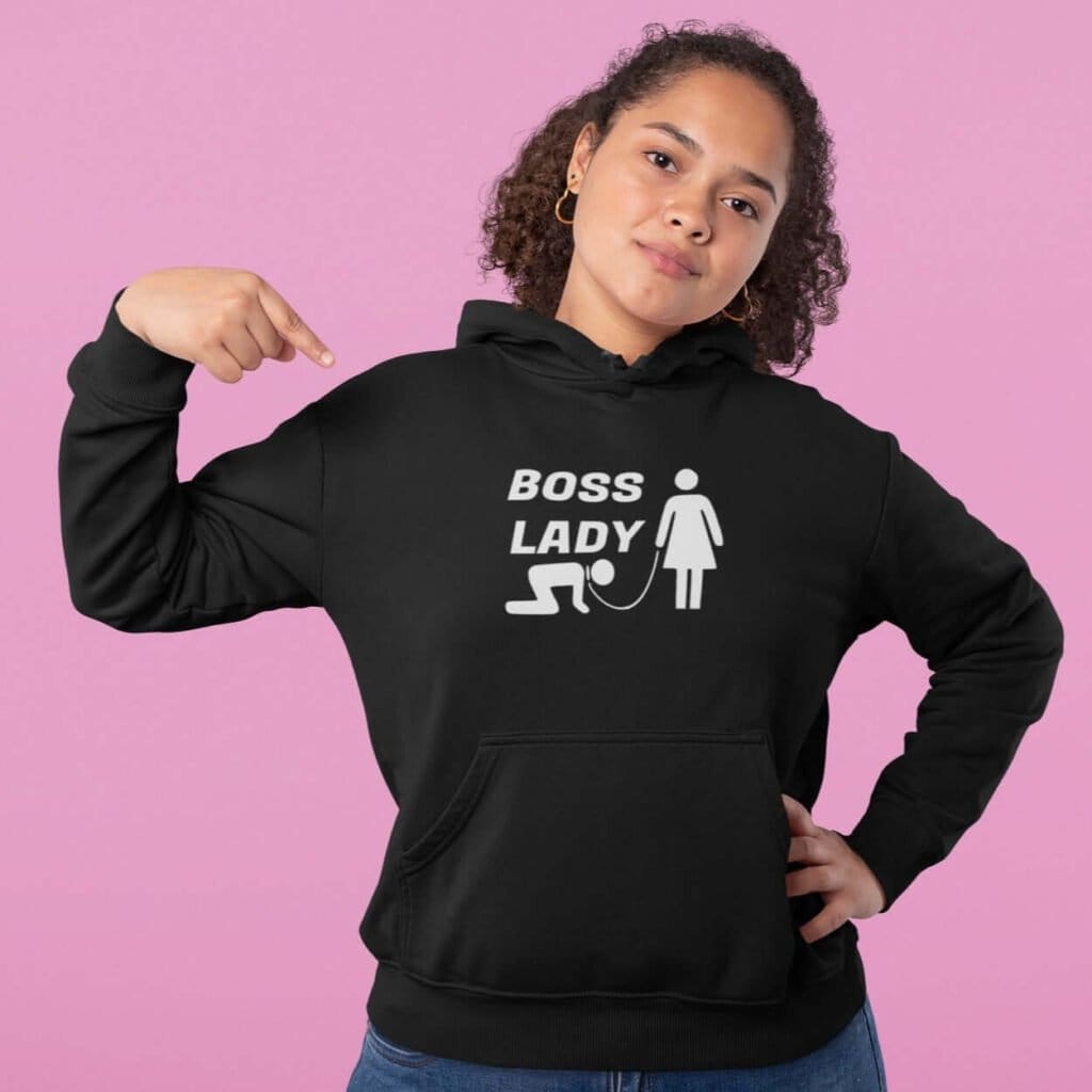 Woman wearing a black hoodie sweatshirt with graphic of collared and leashed man on his hands and knees being led by a woman and the text 'Boss Lady' printed on the front.