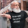Tattooed bearded man wearing black t-shirt with the text 'No one cares that you're offended.' printed on the front.
