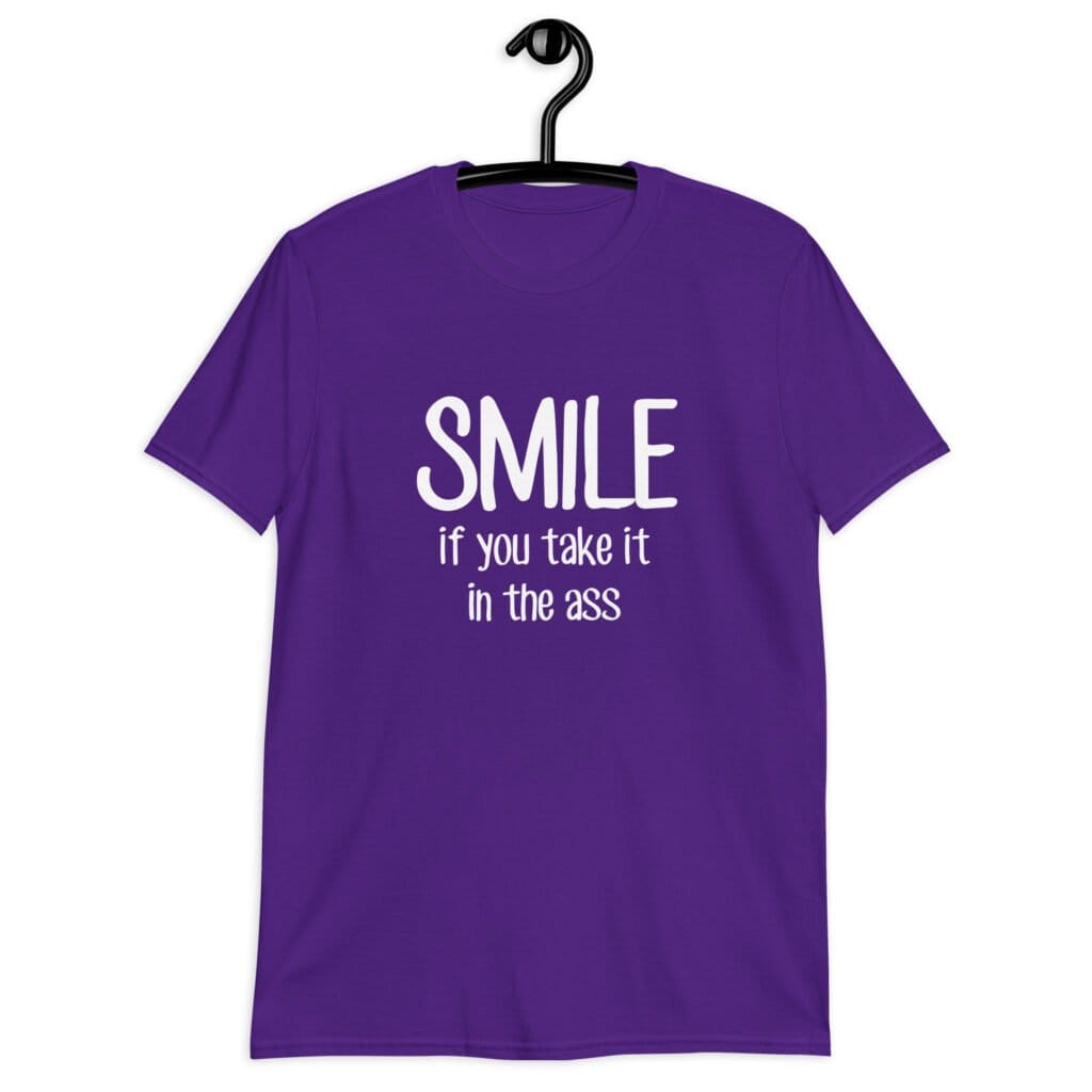 Purple t-shirt with the text 'Smile if you take it in the ass' printed on the front. The word 'smile' is large and the words 'take it in the ass' are much smaller.