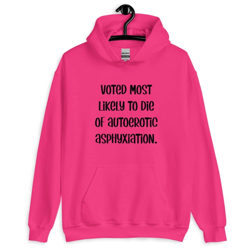 Heliconia pink hoodie sweatshirt with the hood up covering some of her face. The hoodie has the text 'Voted most likely to die of autoerotic asphyxiation.' printed on the front.