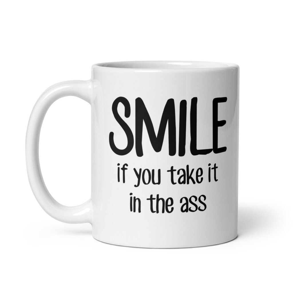 White ceramic mug with the text 'Smile if you take it in the ass' printed on both sides. The word 'smile' is large and the words 'take it in the ass' are much smaller.