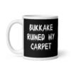 White and black ceramic coffee mug with the text 'Bukkake ruined my carpet' printed in drippy font on both sides.