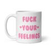 White ceramic coffee mug with the text 'Fuck your feelings' printed on both sides in pink. There are cute pink hearts next to the words.