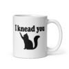 White ceramic coffee mug that has an image of a silhouette of a cat and the text 'I knead you' printed on both sides of the mug.