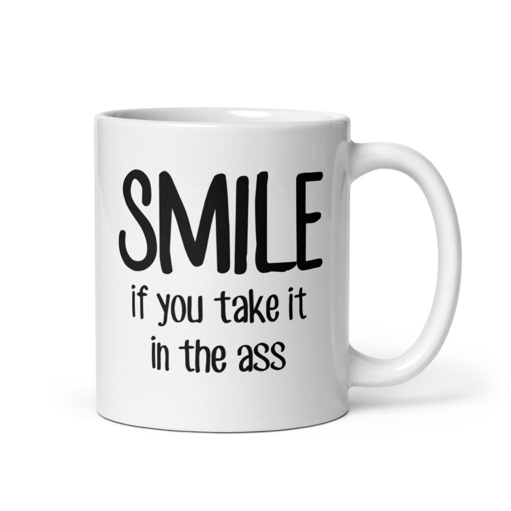 White ceramic mug with the text 'Smile if you take it in the ass' printed on both sides. The word 'smile' is large and the words 'take it in the ass' are much smaller.