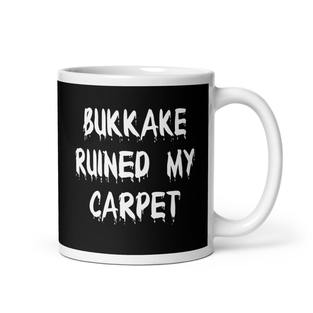 White and black ceramic coffee mug with the text 'Bukkake ruined my carpet' printed in drippy font on both sides.