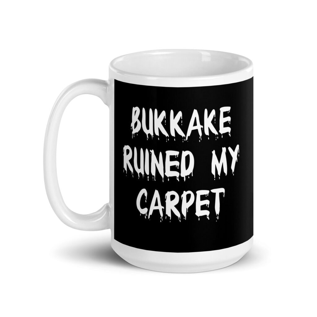 White and black ceramic coffee mug with the text 'Bukkake ruined my carpet' printed in drippy font on both sides.