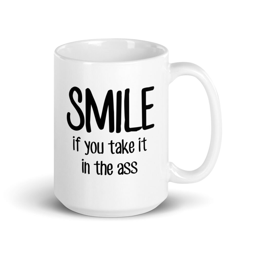 White ceramic mug with the text 'Smile if you take it in the ass' printed on both sides. The word 'smile' is large and the words 'take it in the ass' are much smaller.