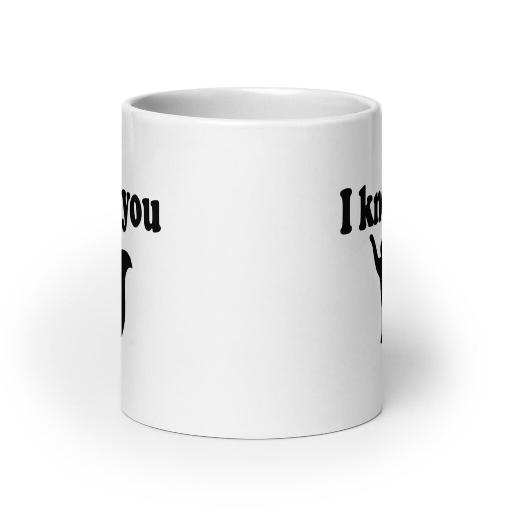 White ceramic coffee mug that has an image of a silhouette of a cat and the text 'I knead you' printed on both sides of the mug.