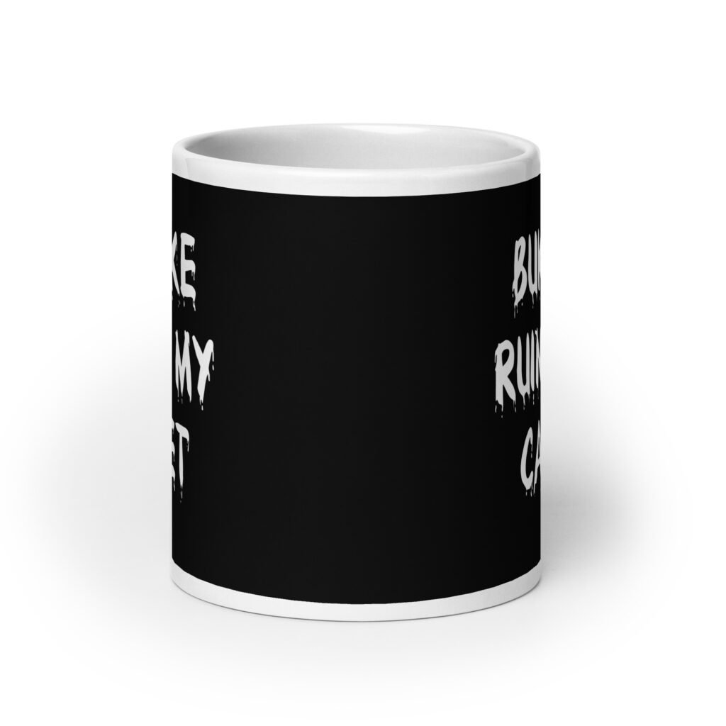 White and black ceramic coffee mug with the text 'Bukkake ruined my carpet' printed in drippy font on both sides.